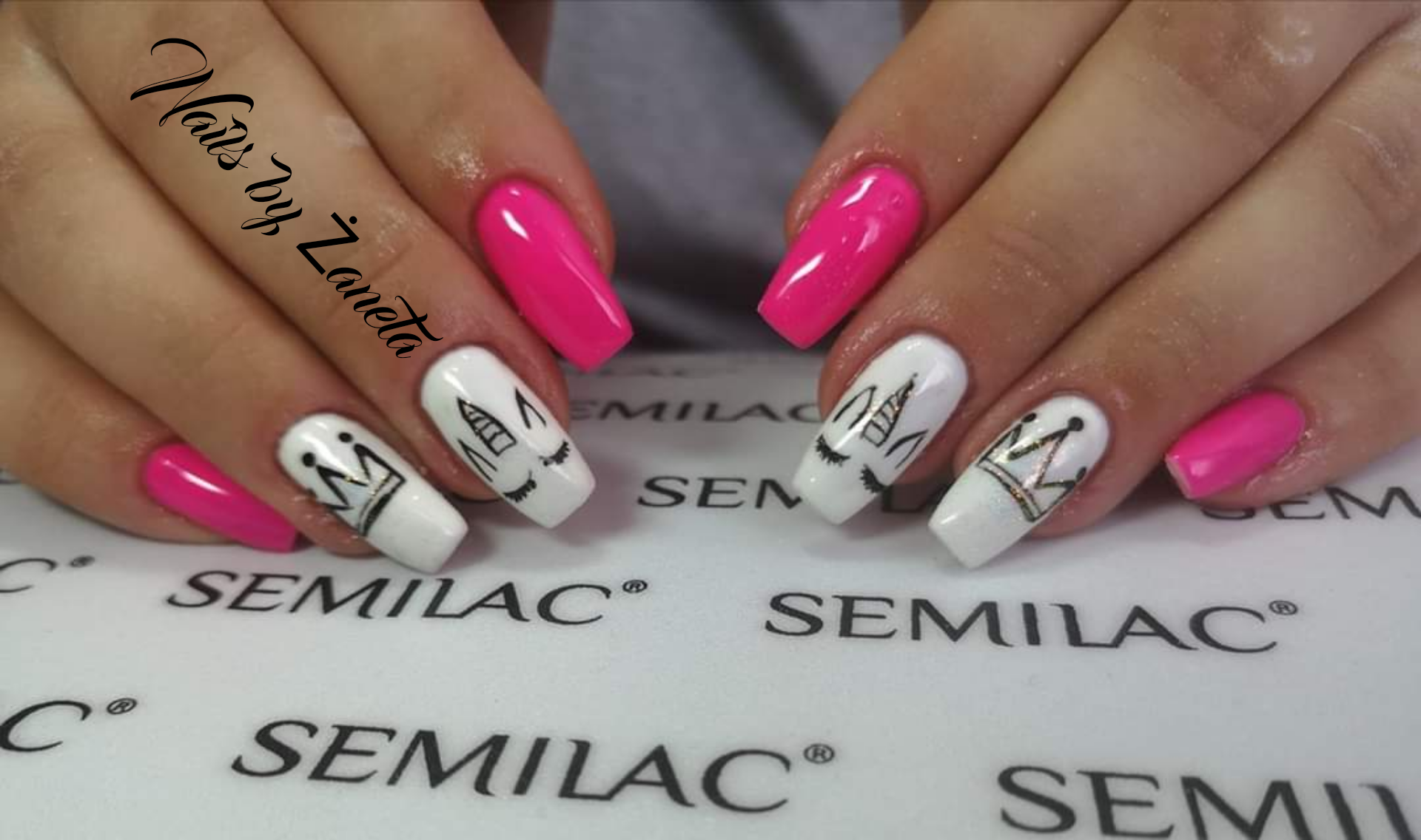 Ręce z pomalowanymi paznokciami: różowe i białe z rysunkami jednorożców i korony na tle logo Semilac.