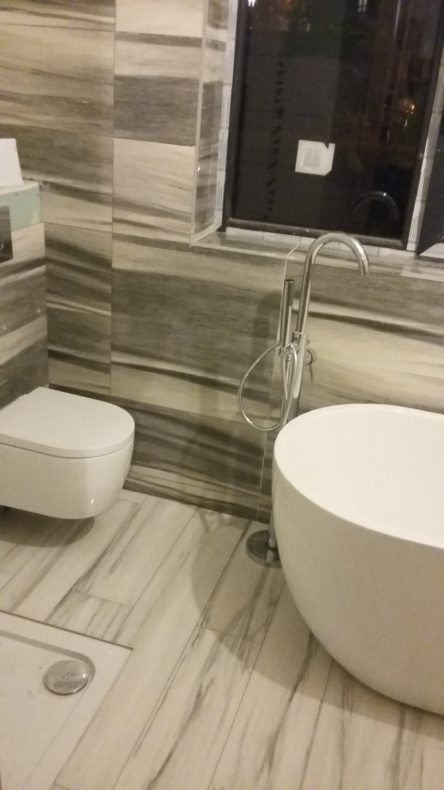 Nowoczesna łazienka z wolnostojącą wanną, podwieszaną toaletą i płytkami imitującymi marmur na ścianach i podłodze, widok z boku.