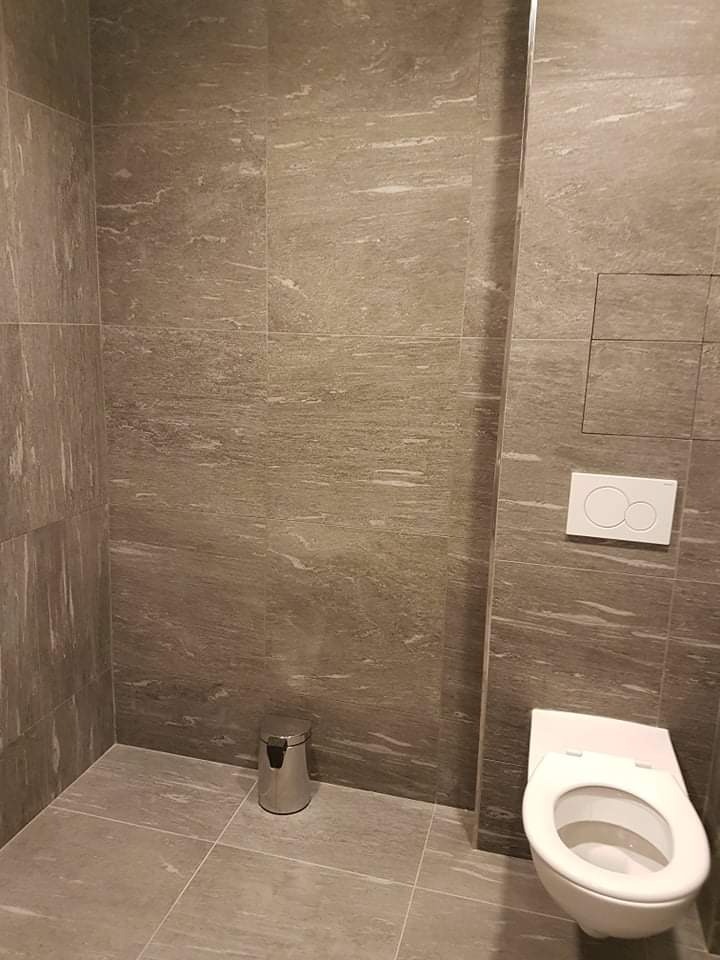 Wykończona łazienka w Kolbuszowej z szarymi płytkami imitującymi kamień, wisząca toaleta i mały metalowy kosz na śmieci.