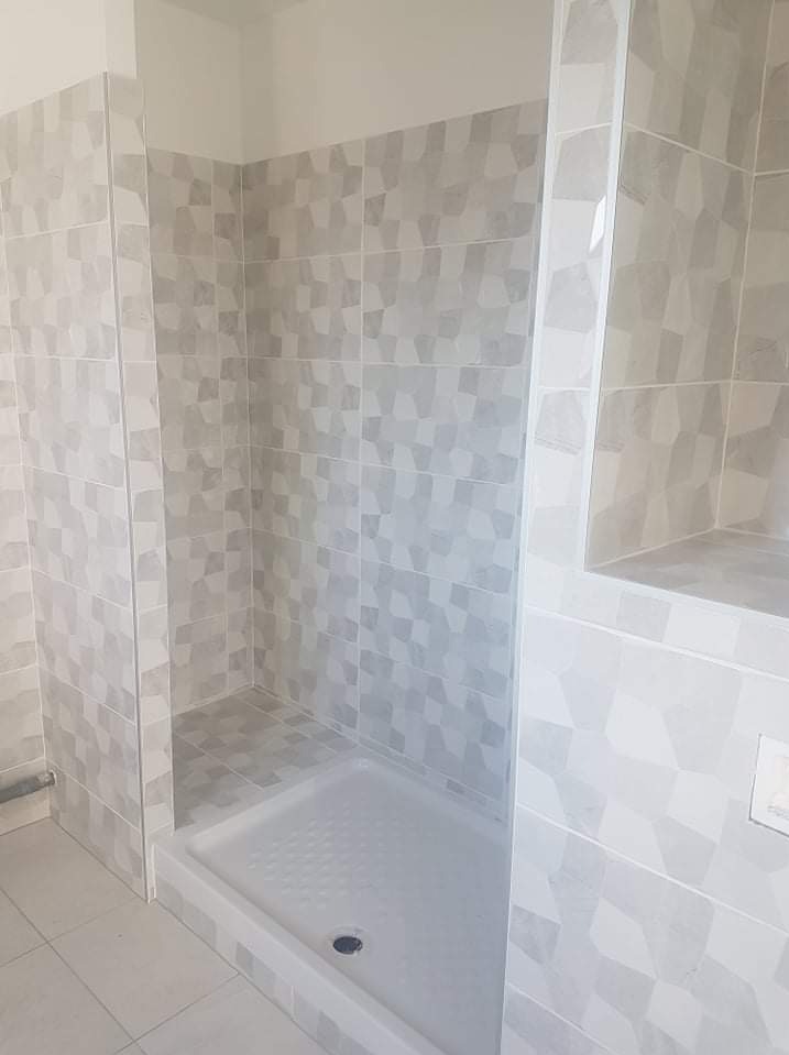Nowoczesna kabina prysznicowa z szarymi, geometrycznymi płytkami; widoczna nisza w ścianie wykończona tym samym wzorem; biały brodzik z odpływem.