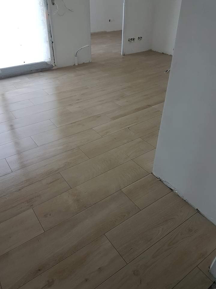 Ułożona pod kątem jasna podłoga z płytek imitujących drewno, widoczne niedokończone ściany i wystające kable.