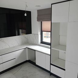 Mebstar - Nowoczesna kuchnia z białymi szafkami, blatem imitującym marmur i czarnymi akcentami. Widoczne okno z roletą i minimalistyczna lampa. Podłoga z płytek imitujących marmur.