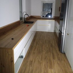 Mebstar - Nowoczesna kuchnia z drewnianym blatem i białymi frontami szafek. Widoczny czarny zlew i bateria. Otwarta szuflada ukazuje mechanizm. Na blacie leży śrubokręt.