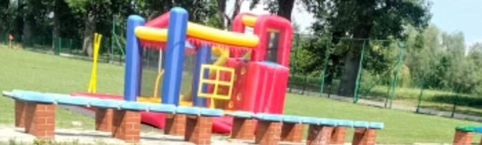 Kolorowy dmuchany zamek z elementami niebieskimi, żółtymi i czerwonymi, ustawiony na trawie w plenerze, z niskim płotkiem z cegieł w pierwszym planie.