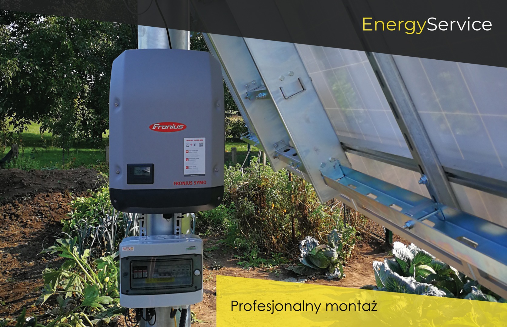 Zamontowany inwerter Fronius SYMO z rozdzielnicą elektryczną na tle ogrodu z kapustą i panelami słonecznymi.