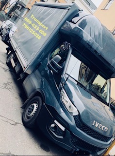 Niebieski samochód dostawczy marki Iveco z plandeką, na której widnieją numery telefonów, zaparkowany na ulicy w mieście.