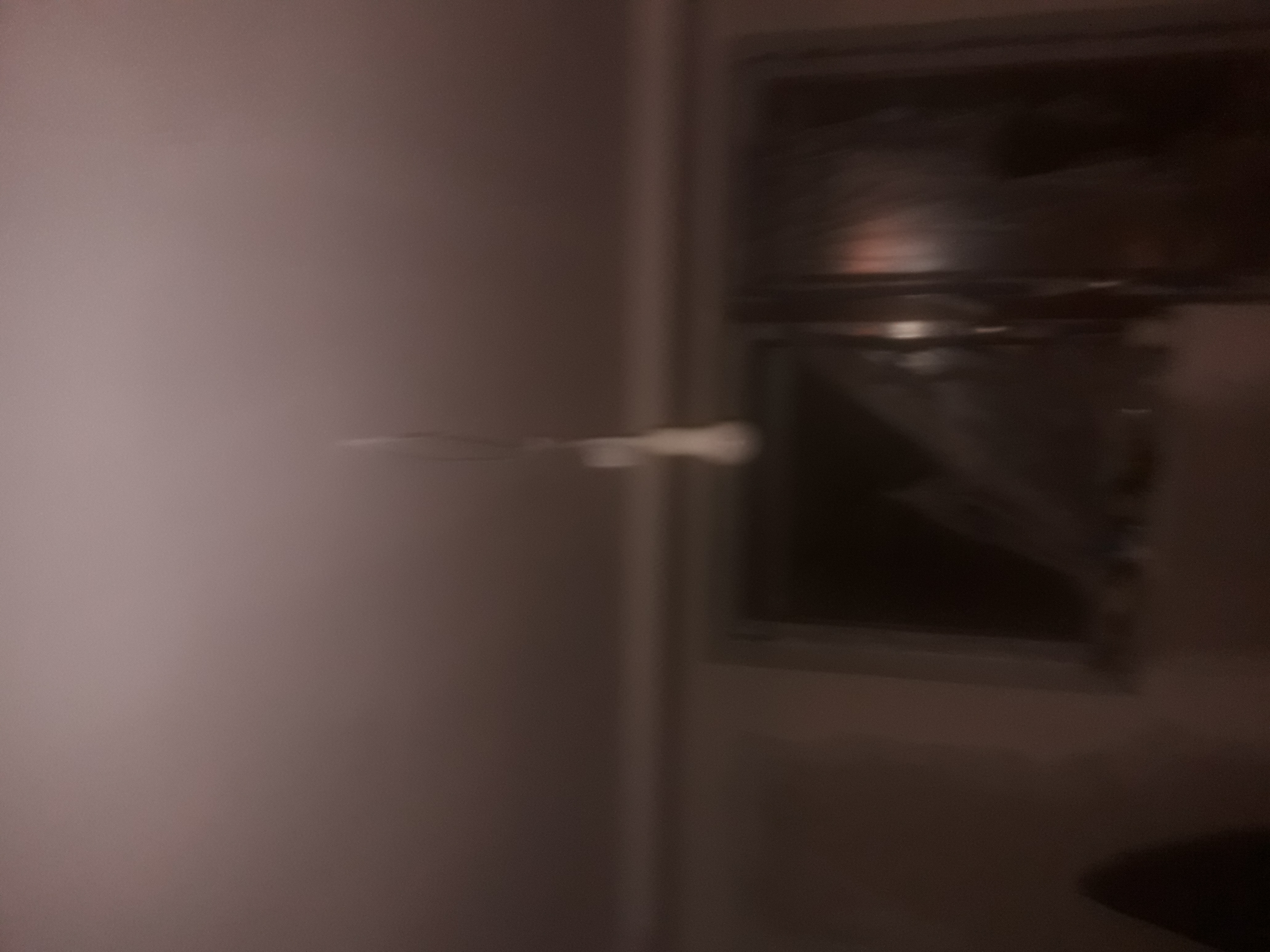 Niedokładne, ciemne zdjęcie ściany po malowaniu, widoczne niedociągnięcia i zacieki farby, z fragmentem okna w tle, wskazujące na potrzebę poprawek.