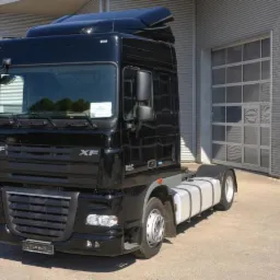 Czarny ciągnik siodłowy DAF XF bez naczepy, zaparkowany przed szarym budynkiem z segmentową bramą garażową.