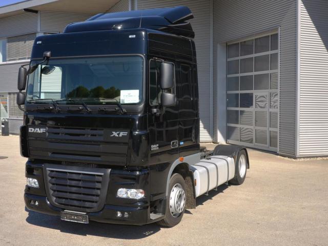Czarny ciągnik siodłowy DAF XF bez naczepy, zaparkowany przed szarym budynkiem z segmentową bramą garażową.