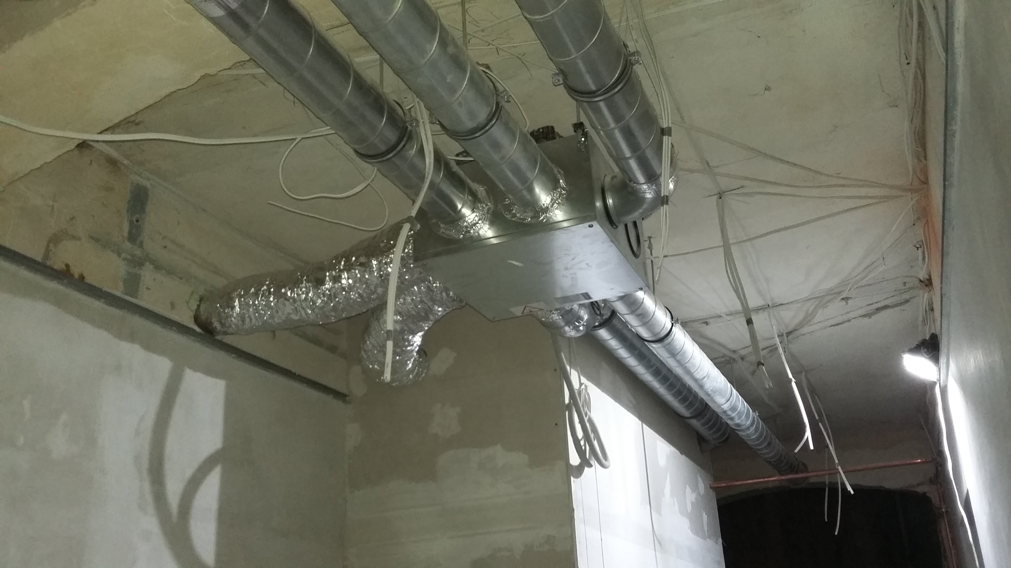 Instalacja systemu wentylacji z metalowych rur w surowym wnętrzu budynku, widoczne przewody i elementy montażowe.