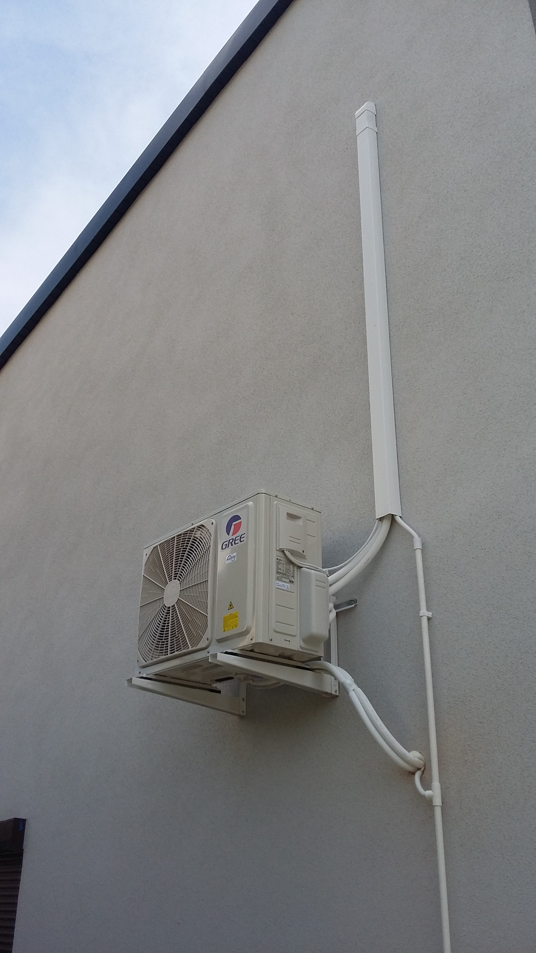 Zewnętrzna jednostka klimatyzacji firmy Gree zamontowana na elewacji budynku z widocznymi przewodami i maskownicą.