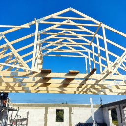 Budujemy z drewna - Konstrukcja drewniana dachu w trakcie budowy domu z bloczków, widok na niebieskie niebo, drabina rusztowania i poziomica przy ścianie.