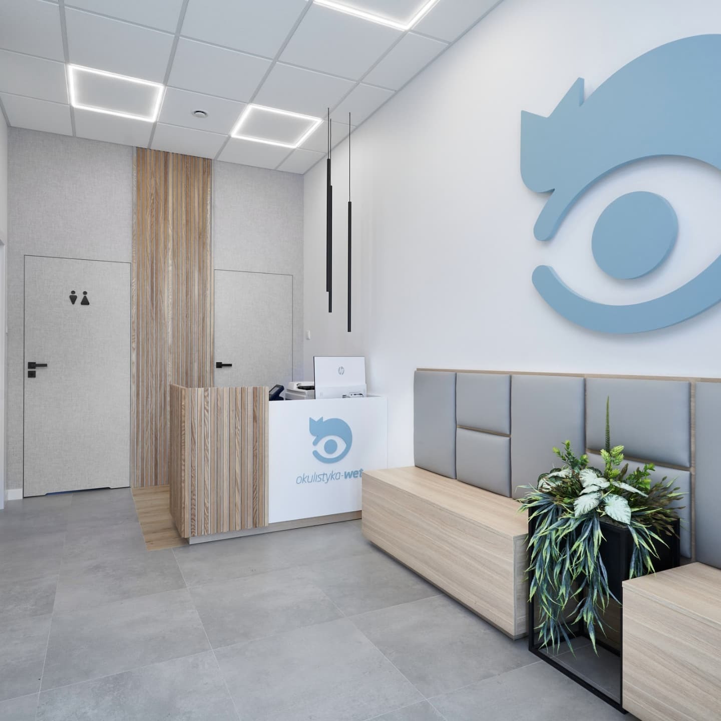 Nowoczesne wnętrze poczekalni: szara podłoga, drewniana lada recepcyjna z logo okulistycznym, drewniana ławka z szarym tapicerowanym oparciem, minimalistyczne lampy wiszące i duże logo na ścianie.