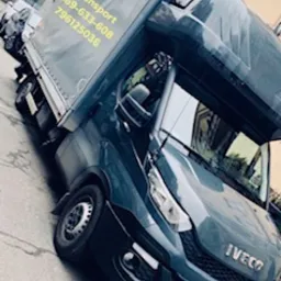 Ciemny samochód dostawczy Iveco z plandeką i numerami telefonów na boku, zaparkowany na ulicy w mieście.