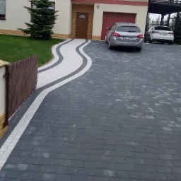 Ułożona kostka brukowa w miejscowości Góra tworząca falujący wzór podjazdu do domu z dwoma samochodami w tle.