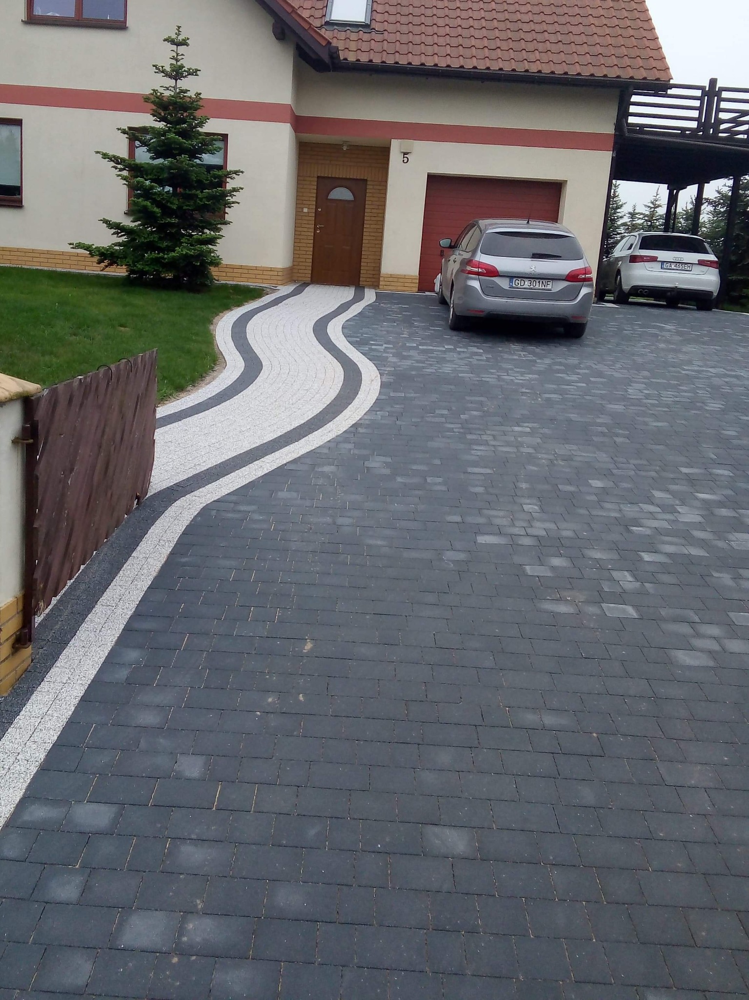 Ułożona kostka brukowa w miejscowości Góra tworząca falujący wzór podjazdu do domu z dwoma samochodami w tle.