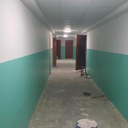 walldone - Korytarz w trakcie malowania, ściany pomalowane do połowy na zielono, powyżej białe, widoczne otwarte drzwi i stołek malarski.