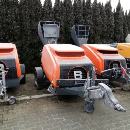 Pompy do betonu marki Putzmeister, pokryte szronem, ustawione na placu z tujami w tle.