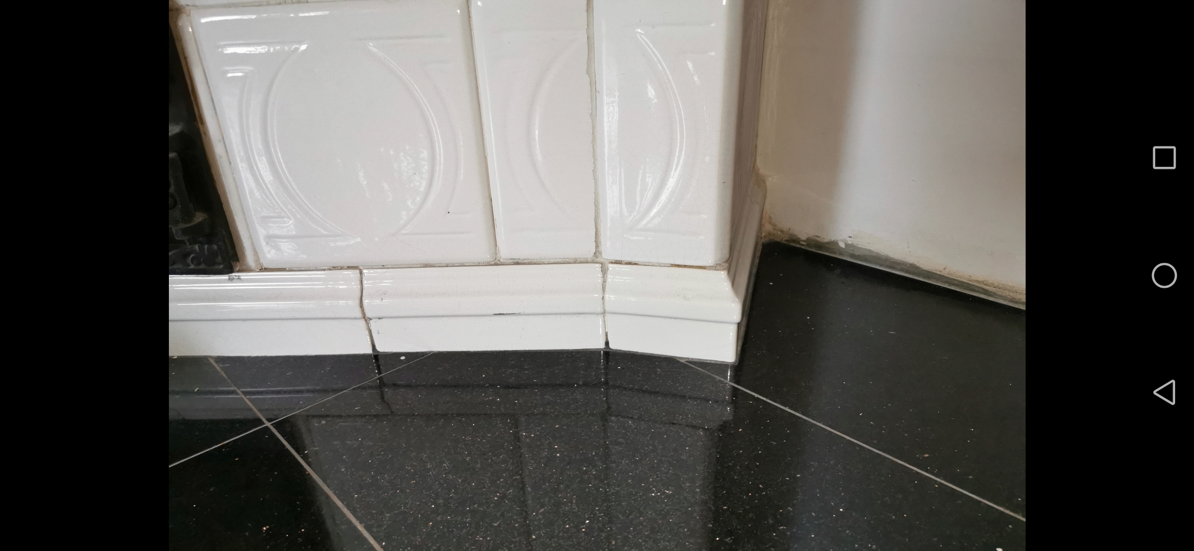 Białe, dekoracyjne płytki ceramiczne z zaokrąglonym wzorem, ułożone na ścianie w rogu, z czarną, błyszczącą podłogą z delikatnym brokatem w tle.