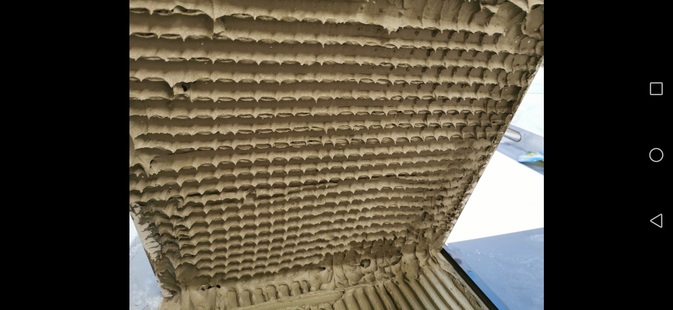 Świeżo nałożona warstwa zaprawy klejowej na płytkę, widoczne charakterystyczne rowki i wypustki.