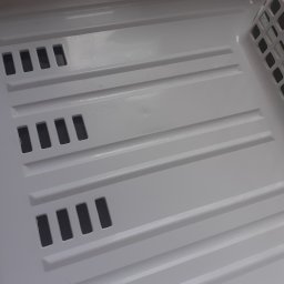 JUŻ w PORZĄDKU - Wnętrze czystej, białej kuwety z kratką, prawdopodobnie po sprzątaniu. Widoczne ślady wody i poziome przetłoczenia.