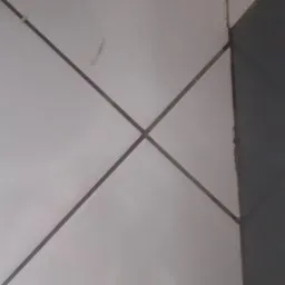 Białe, błyszczące płytki ułożone w karo z ciemną fugą, fragment ciemnej płytki po prawej. Minimalistyczne ujęcie detalu wyczyszczonej powierzchni.