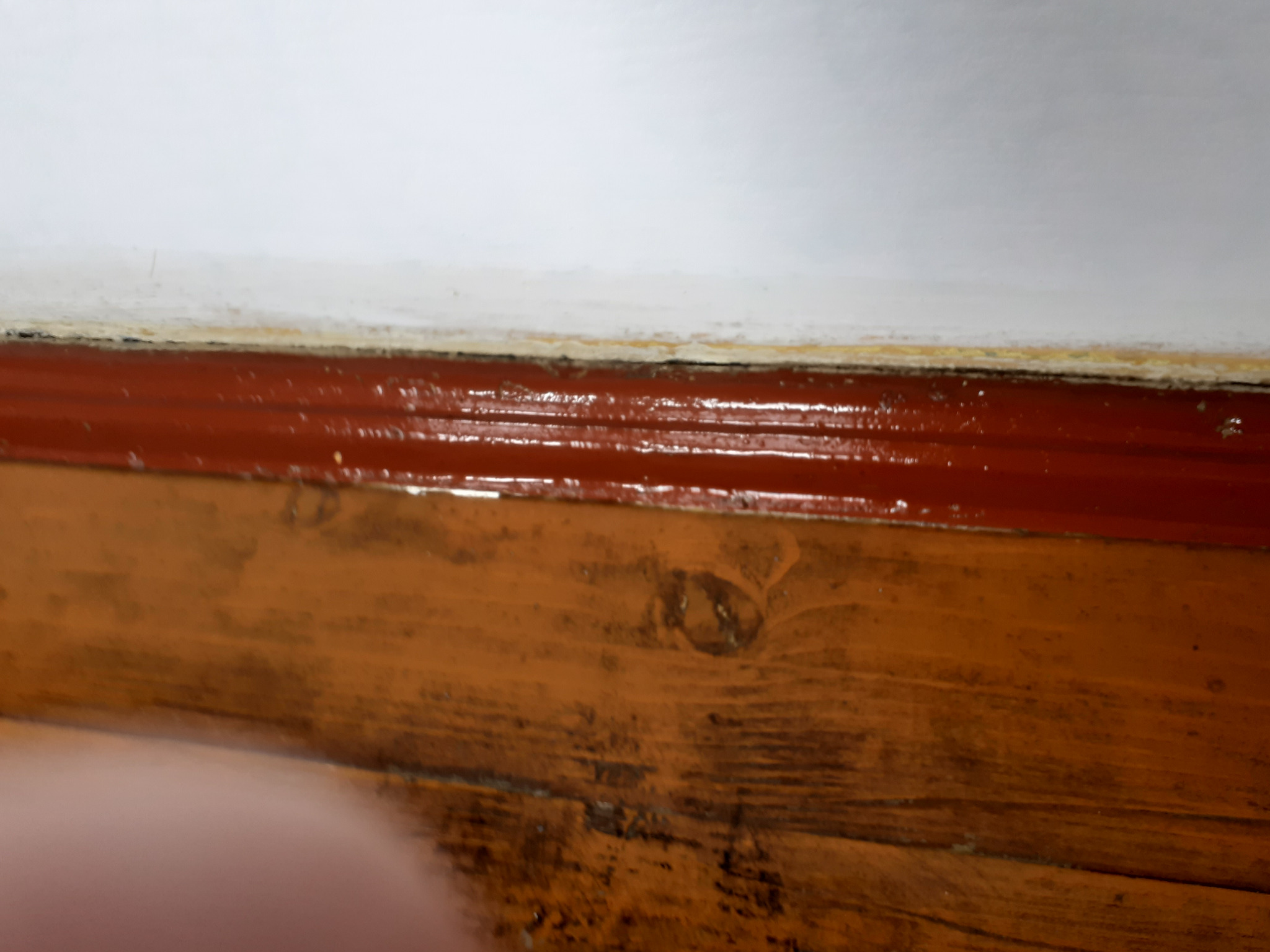 Detail podłogi po sprzątaniu: drewniana podłoga, czerwona listwa przypodłogowa i biała ściana. Widoczne ślady czyszczenia.