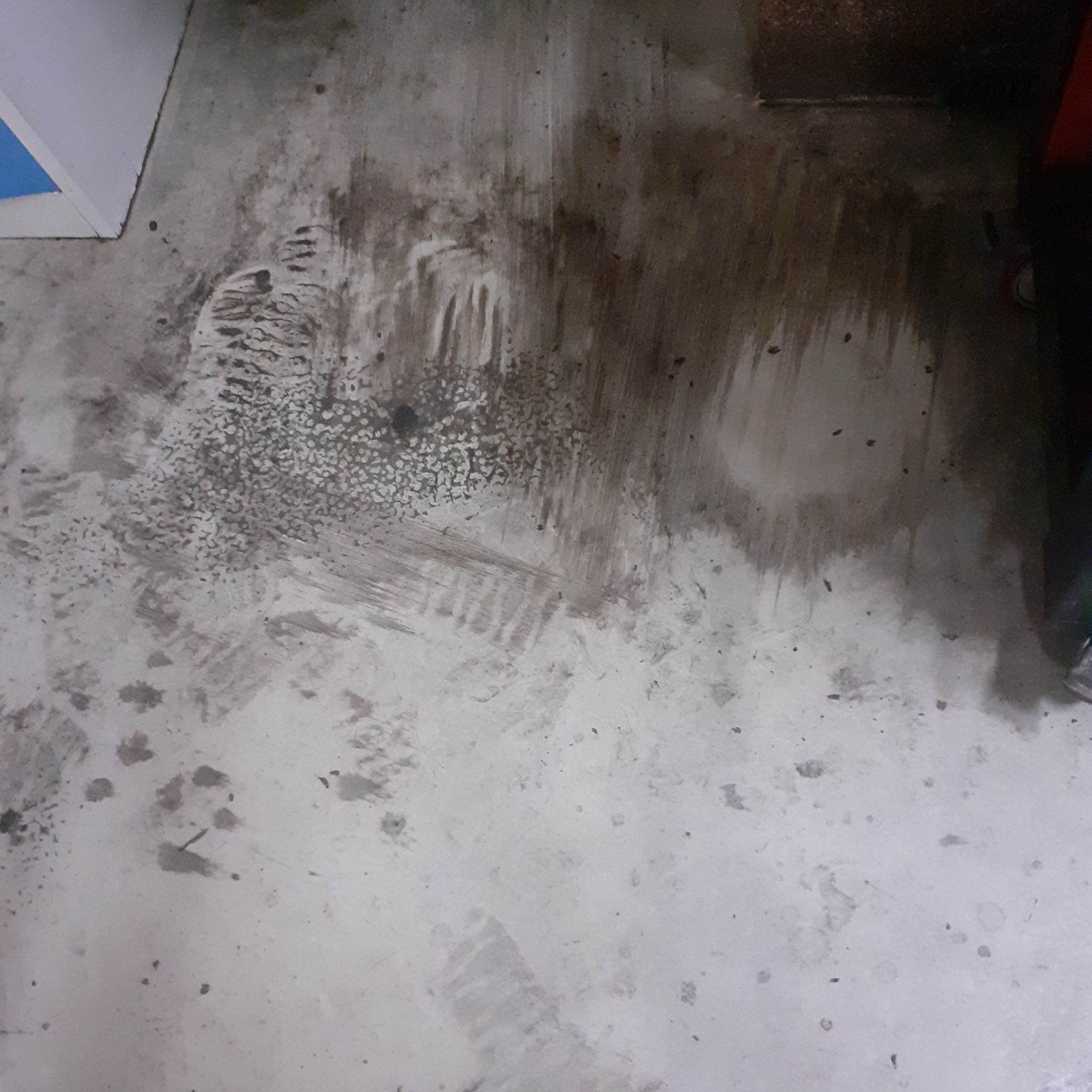 Zabrudzona, betonowa podłoga w bliskim ujęciu, z widocznymi plamami i śladami po czyszczeniu, ukazująca trudne do usunięcia zabrudzenia.