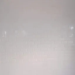 Ściana łazienki wyłożona błyszczącymi, białymi płytkami typu metro, z widocznymi otworami na instalacje wodno-kanalizacyjne i fragmentem ściany w trakcie przygotowania do dalszych prac.