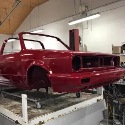 Czerwony, odnowiony szkielet kabrioletu Volkswagen Golf Mk1 na wózku warsztatowym w jasnym pomieszczeniu, przygotowany do dalszych prac.