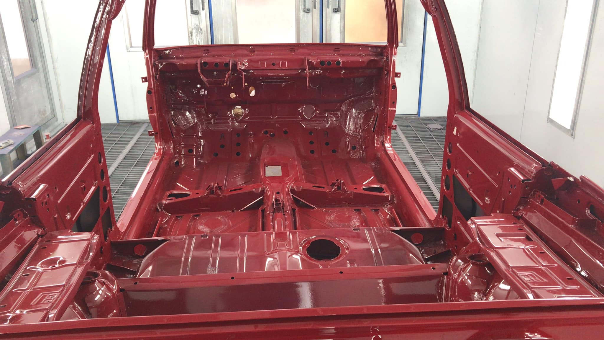 Czerwona karoseria samochodu po lakierowaniu, widok wnętrza bez wyposażenia, w kabinie lakierniczej.