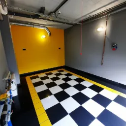 Wykończone wnętrze garażu w Katowicach z podłogą w szachownicę z czarno-białych płytek, ż&oacute;łtą obw&oacute;dką i ż&oacute;łtą ścianą, szara ściana z rurami miedzianymi i instalacją elektryczną.