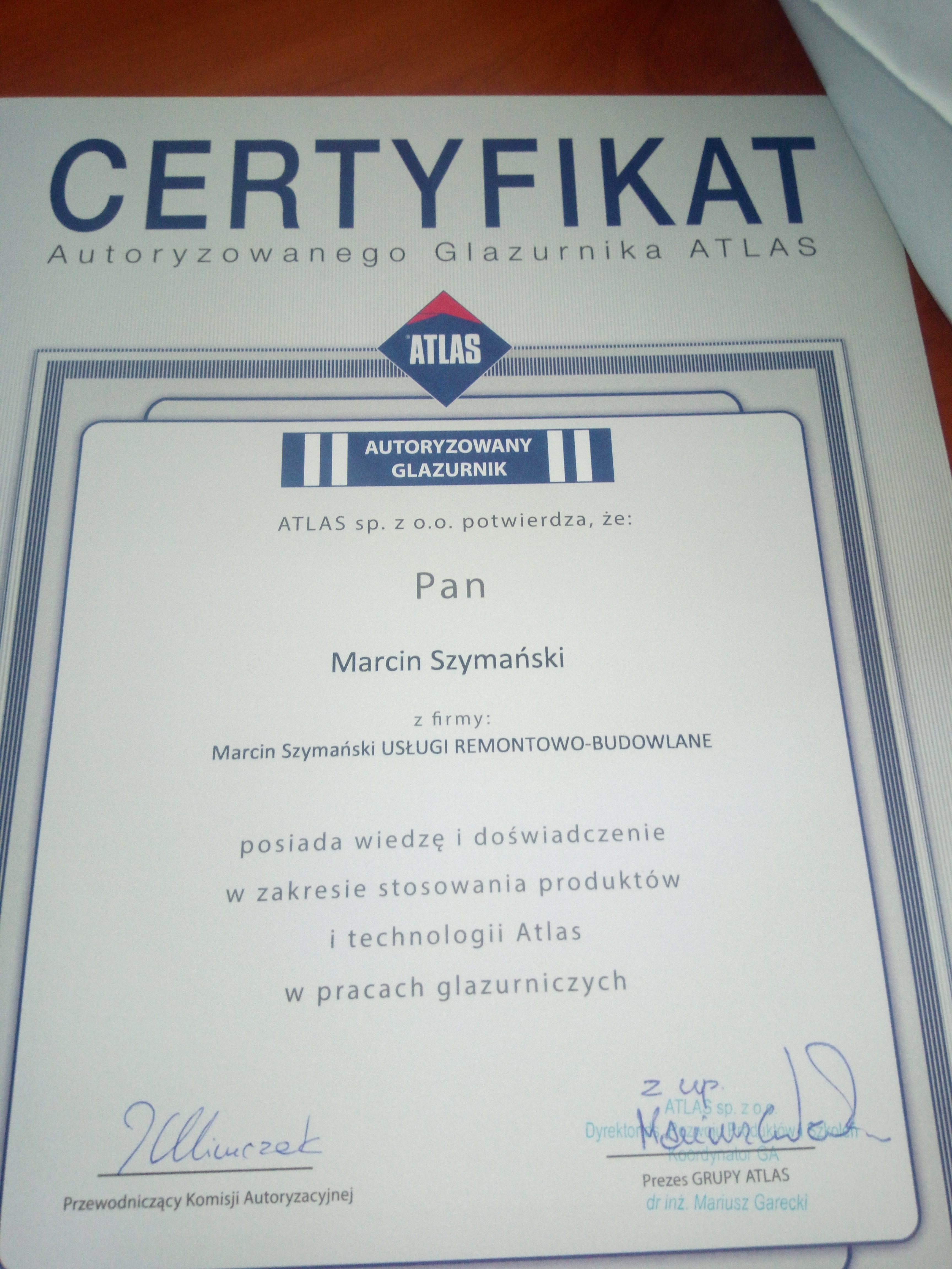 Certyfikat Autoryzowanego Glazurnika Atlas dla Marcina Szymańskiego, potwierdzający wiedzę i doświadczenie w stosowaniu produktów i technologii Atlas w pracach glazurniczych, z podpisami...