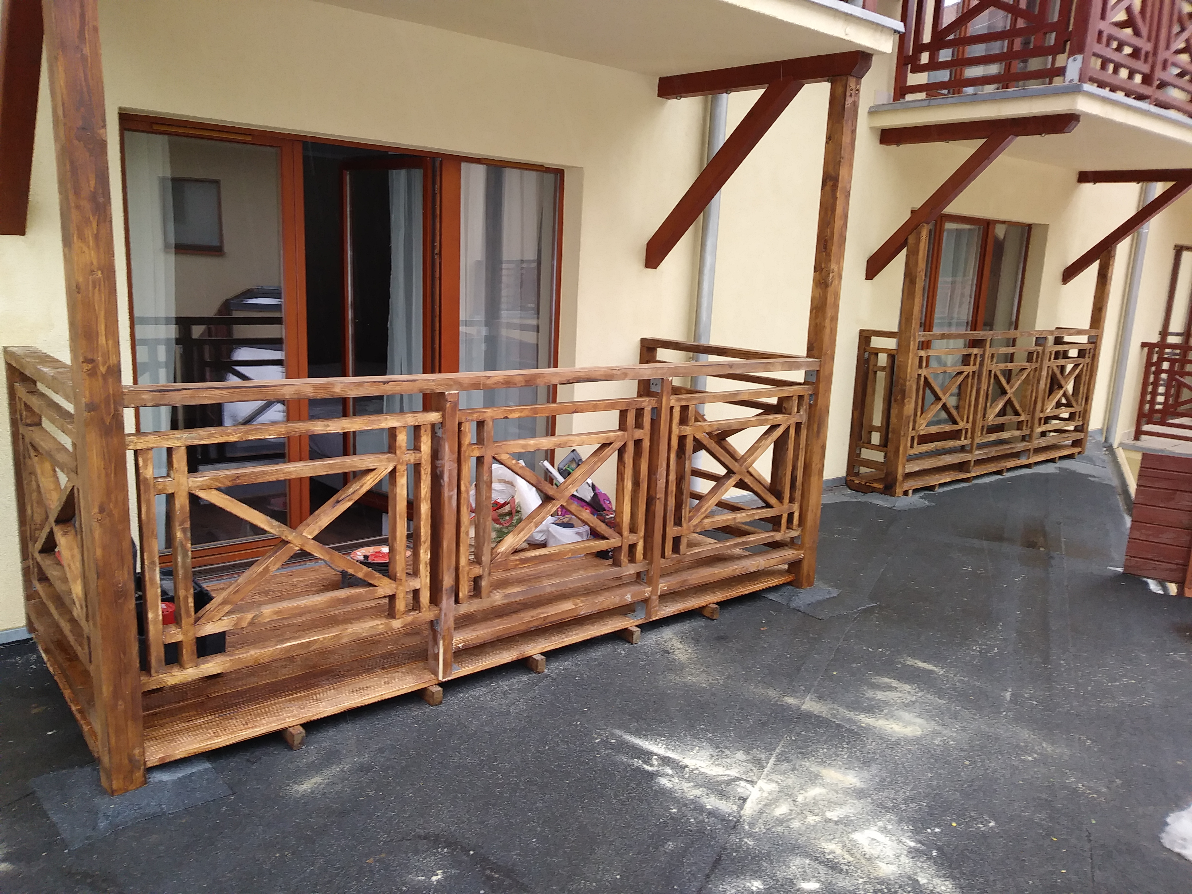 Drewniane balustrady balkonowe z krzyżowymi wzorami, świeżo po impregnacji, w Jeleniej Górze. Widoczne detale konstrukcyjne i faktura drewna.
