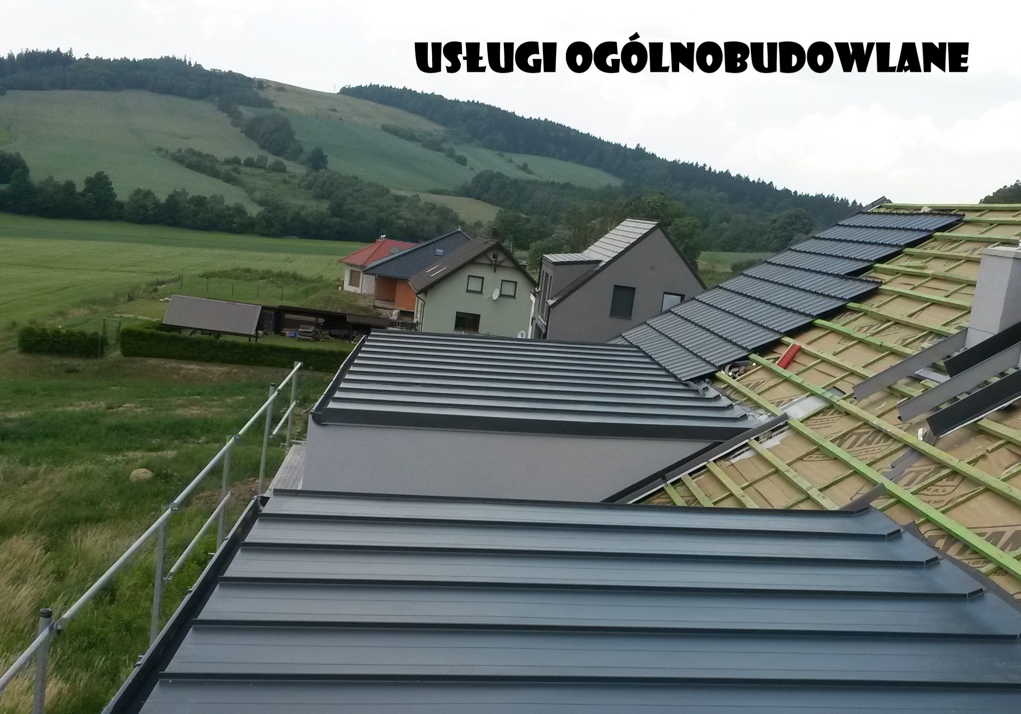 Nowy, szary dach z blachy na tle zielonych wzgórz i zabudowań, widoczne elementy konstrukcji drewnianej i fragmenty zabezpieczeń.