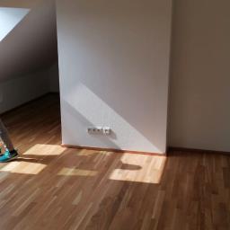 SPIC AND SPAN. Home & Office Cleaning - Osoba w szarych spodniach i białej koszulce myje okno dachowe w pustym pokoju; na podłodze stoi butelka ze środkiem czyszczącym.