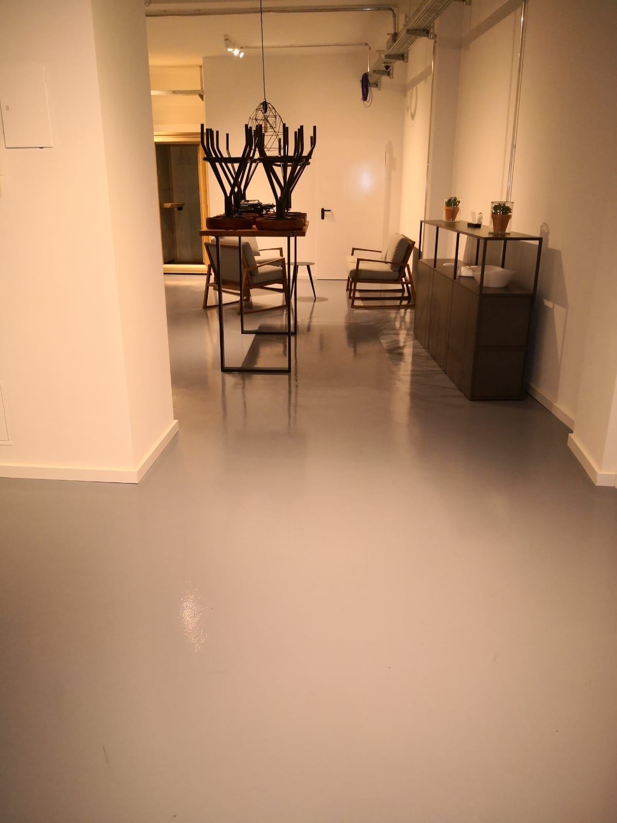 Minimalistyczne wnętrze biurowe z szarą, połyskliwą podłogą, nowoczesnymi meblami i oświetleniem, krzesła ustawione na stole, sugerujące porządkowanie przestrzeni.