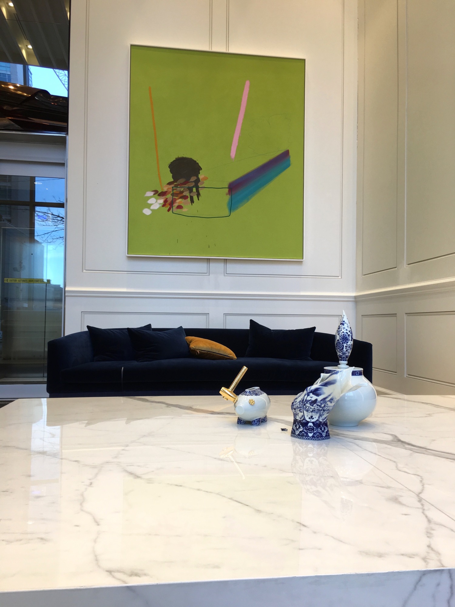 Eleganckie wnętrze z ciemnoniebieską sofą, marmurowym stolikiem i dekoracyjnymi wazonami w stylu Delft na tle ściany z boazerią i abstrakcyjnym obrazem.