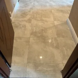 Ułożona podłoga z płytek ceramicznych w odcieniach beżu i szarości, widok z perspektywy wejścia do pomieszczenia, z widocznymi listwami przypodłogowymi i fragmentem progu.