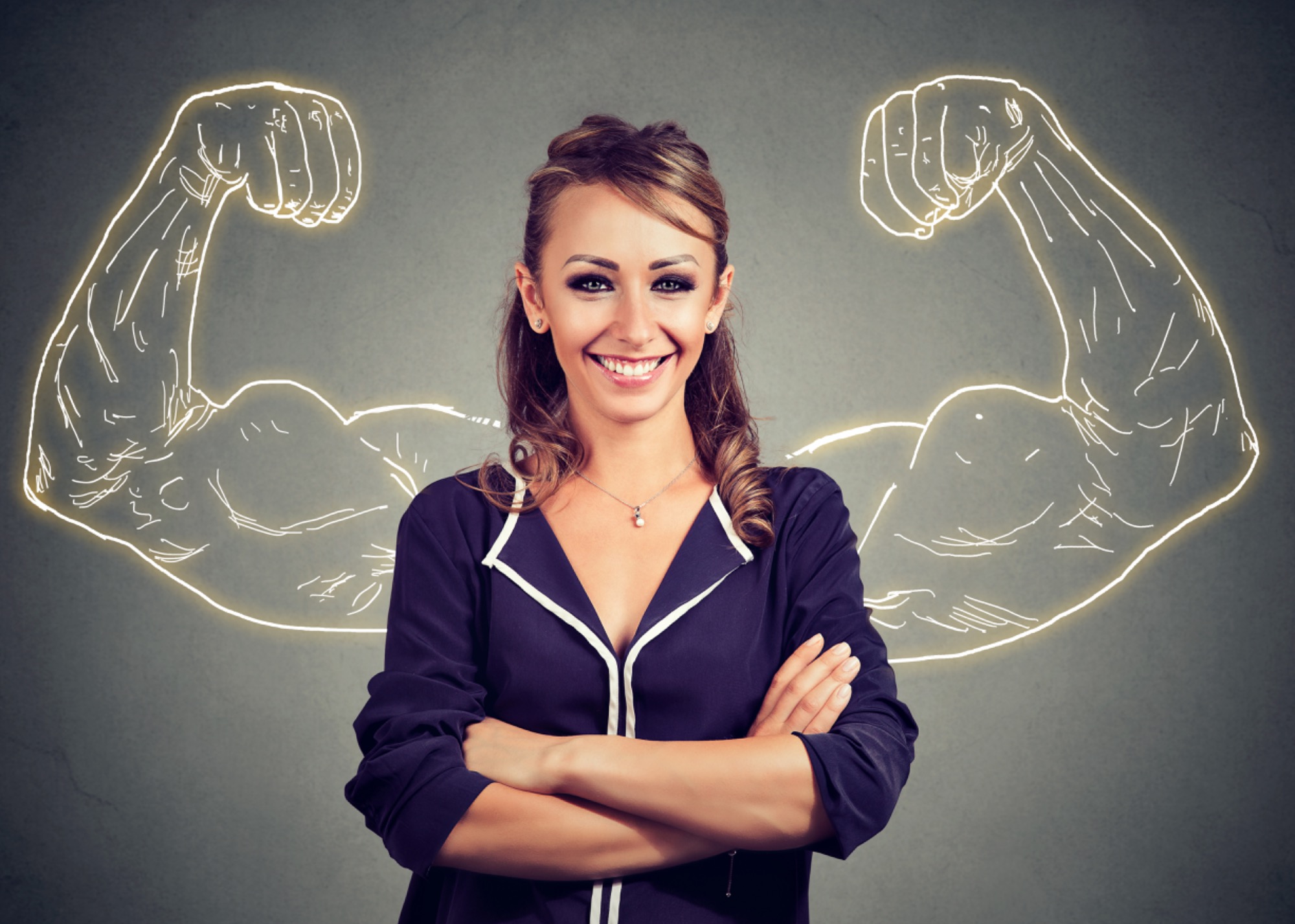 Uśmiechnięta kobieta w granatowej bluzce z białym wykończeniem, ze skrzyżowanymi rękami, na szarym tle z narysowanymi świetlistymi bicepsami, sugerująca siłę i pewność siebie.