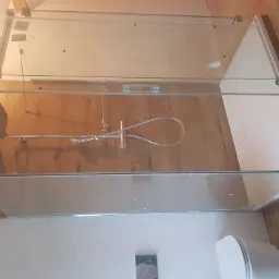 Nowoczesna kabina prysznicowa z chromowaną deszczownicą i odpływem liniowym, widok z góry na drewnopodobne płytki podłogowe i białą miskę WC.