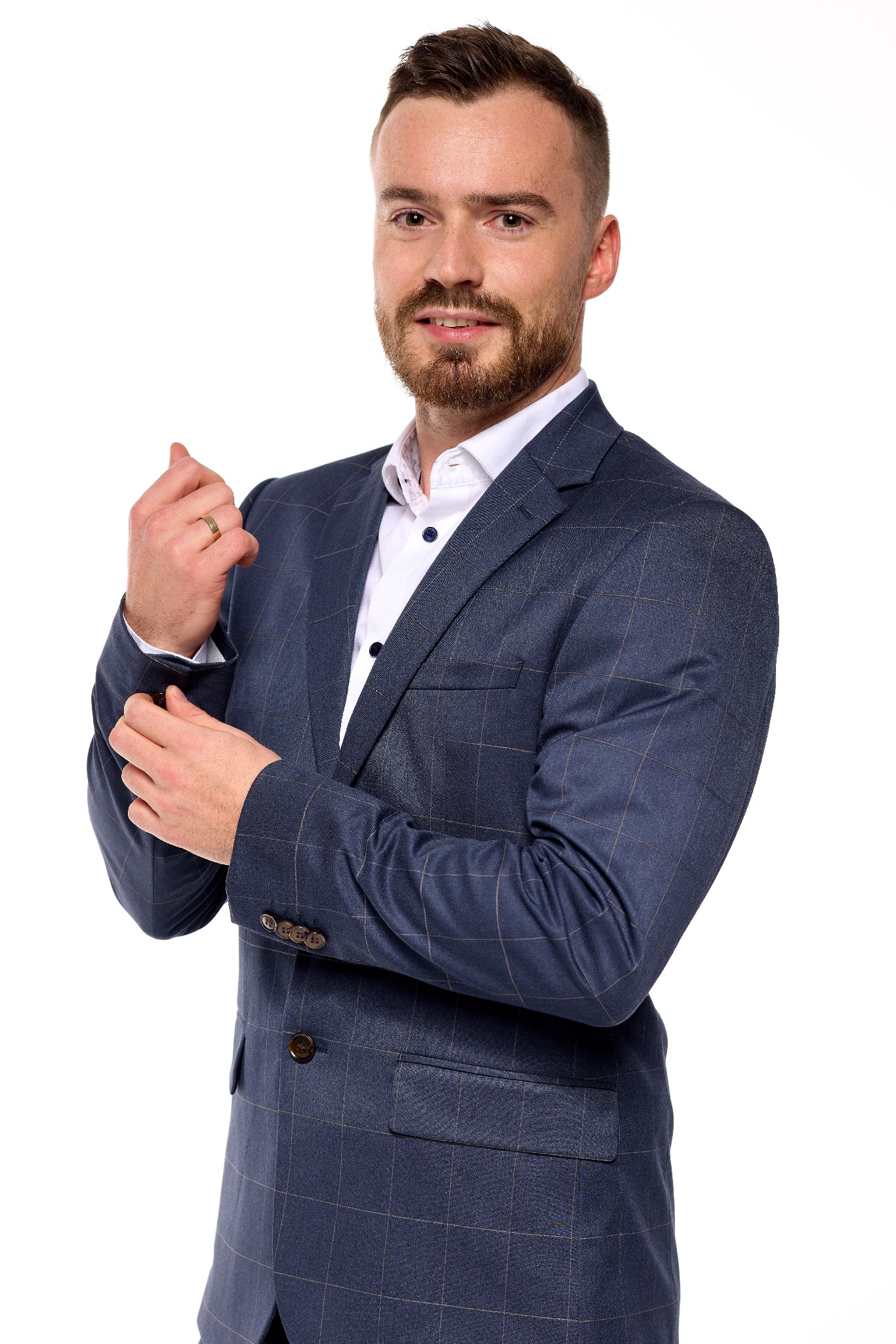 Portret mężczyzny w granatowej marynarce w kratę i białej koszuli, poprawiającego mankiet, na białym tle.