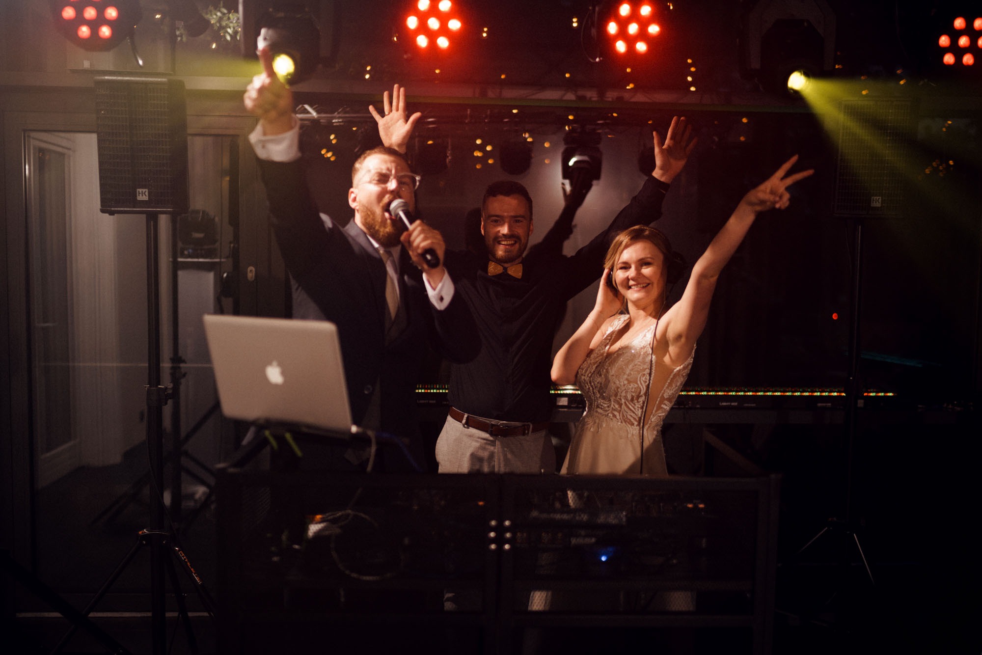 Zespół muzyczny z wokalistą i DJ-ką w trakcie występu na scenie, oświetlenie sceniczne w tle, laptop na statywie.