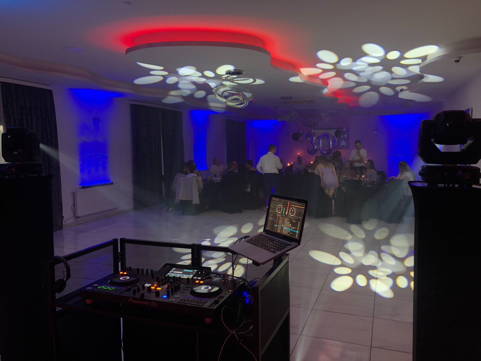 Ustawiony sprzęt DJ-ski z laptopem w Sosnowcu, oświetlenie parkietu w geometryczne wzory podczas imprezy.