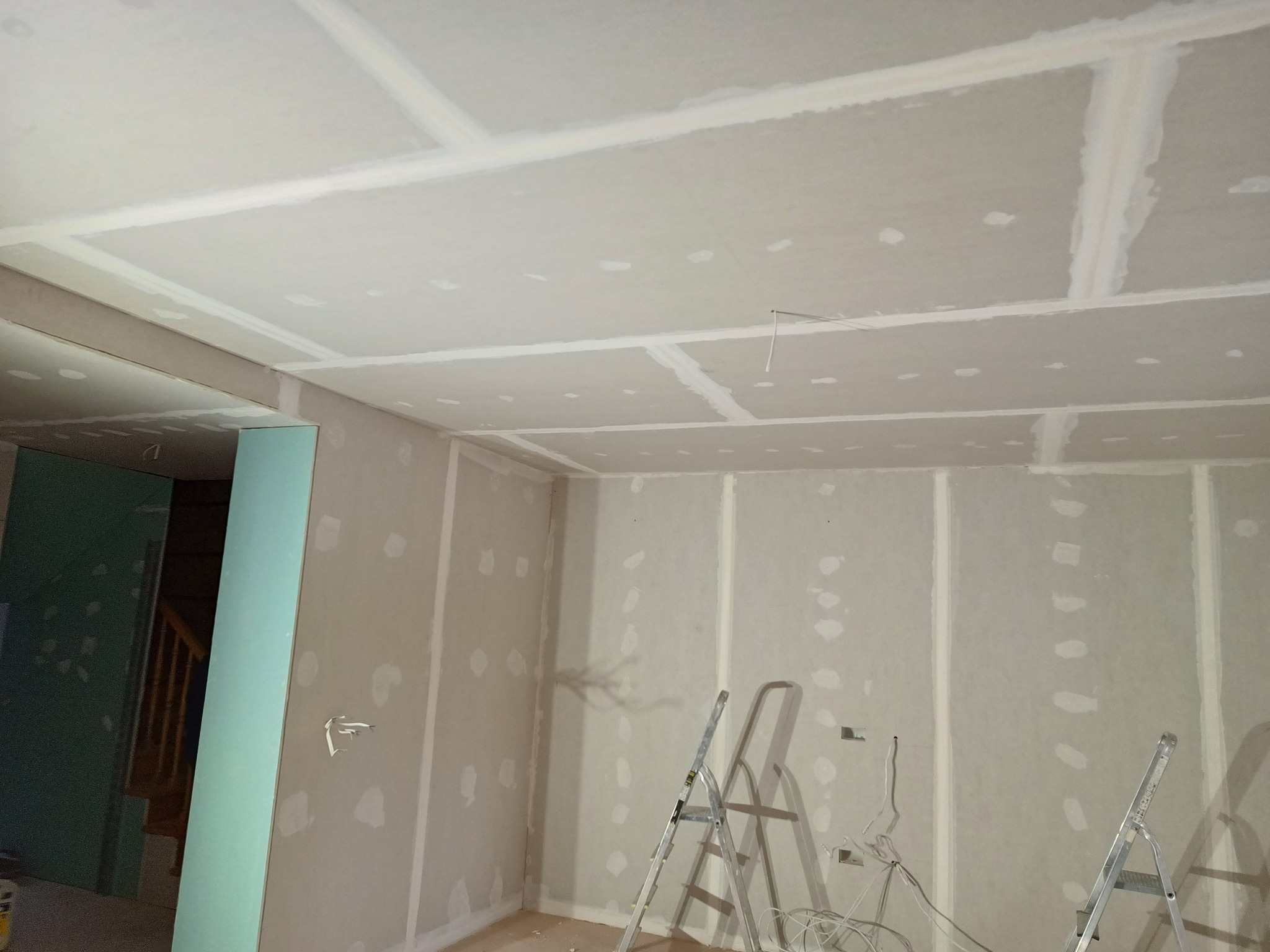 Wnętrze w trakcie remontu: ściany i sufit pokryte płytami z widocznymi łączeniami przed dalszą obróbką, drabiny rozstawione w pomieszczeniu.