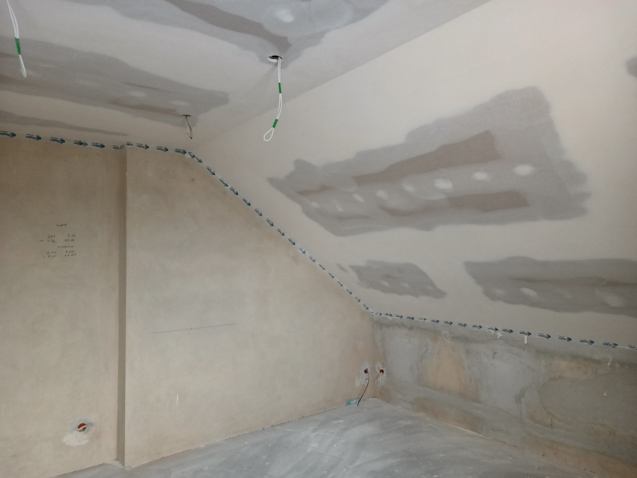 Skośne poddasze w trakcie prac wykończeniowych, widoczne fragmenty ścian i sufitu po wstępnym wyrównaniu, z zaznaczoną linią poziomą taśmą maskującą, przygotowane do dalszych prac.