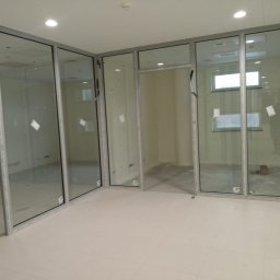 M-Stal Bartosz Mazik - Nowoczesne, przeszklone ścianki działowe z aluminiowymi ramami, tworzące przestrzeń biurową. Widoczne detale mocowań i jasna kolorystyka wnętrza.