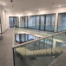 M-Stal Bartosz Mazik - Szklana balustrada schodowa z metalowymi elementami, widok z góry na jasne wnętrze z dużymi oknami. Minimalistyczny design, nowoczesne wykończenie.