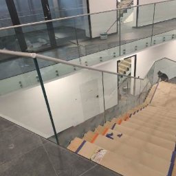 M-Stal Bartosz Mazik - Szklane balustrady na schodach w nowoczesnym wnętrzu. Widoczne zabezpieczone stopnie schodów i jasne, przestronne otoczenie z dużymi oknami.