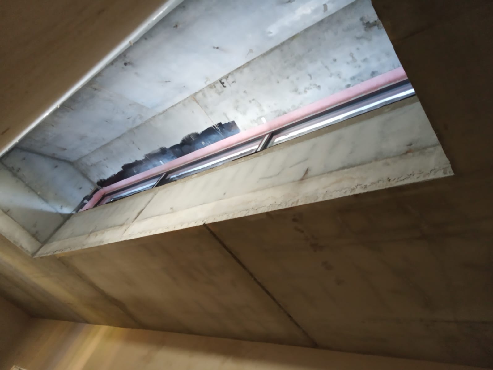 Surowy strop z otworem okiennym i czerwoną rurą wentylacyjną. Widok z dołu, podkreślający industrialny charakter wnętrza w trakcie budowy.